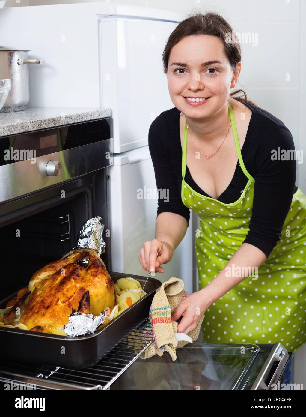 cheerful woman roasting cockerel for dinner